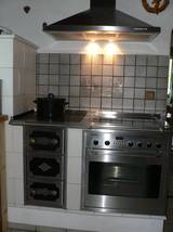 Auf der anderen Seite des Durchganges von der Kche in das Wohnzimmer, nimmt eine Kombination aus Elektroherd, Holzherd und Backfach, alles eingemauert und mit Kacheln verkleidet den Rest der Sdwand der Kche ein.